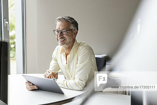 Lächelnder Geschäftsmann mit digitalem Tablet im Büro sitzend