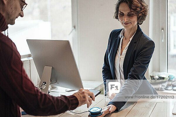 Man paying through bar code being held by smiling woman at counter