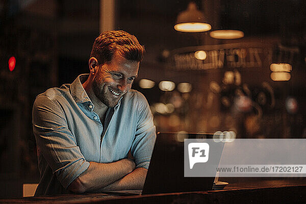 Lächelnder Geschäftsmann  der einen Laptop benutzt  während er in einem Café sitzt