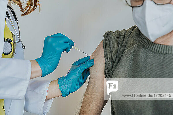 Arzt verabreicht COVID-19-Impfstoff in den Arm eines Patienten im Untersuchungsraum