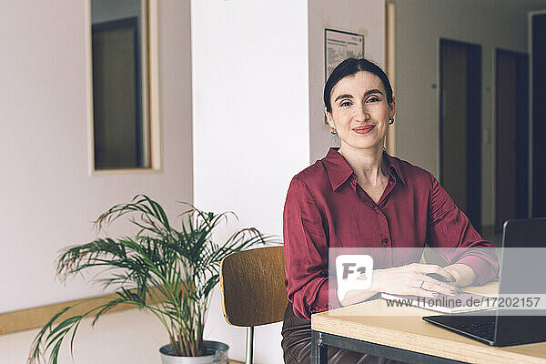 Lächelnde Geschäftsfrau sitzt mit Tagebuch und Laptop am Tisch