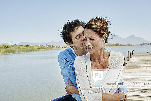 Älterer Mann küsst und umarmt Frau auf der Seebrücke