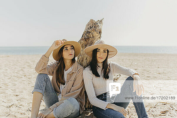 Weibliche Zwillinge sitzen Seite an Seite am Strand an einem sonnigen Tag