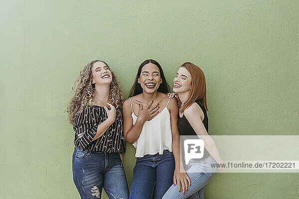 Carefree young women laughing while standing against green wall