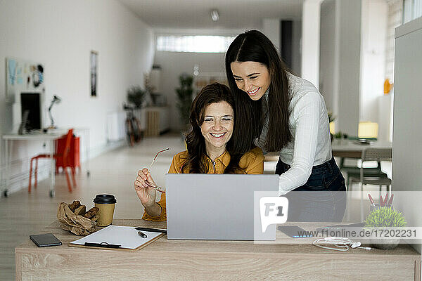 Lächelnde Mutter und Tochter arbeiten an einem Laptop am Schreibtisch im Heimbüro
