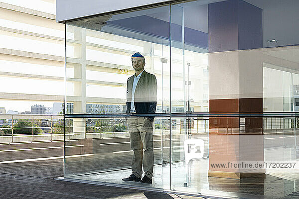 Selbstbewusster Geschäftsmann mit Händen in den Taschen  der in einem modernen Büro am Fenster steht