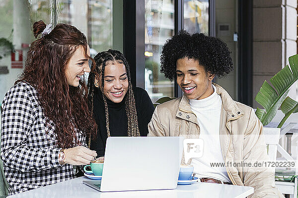 Studenten benutzen einen Laptop  während sie in einem Straßencafé zusammensitzen