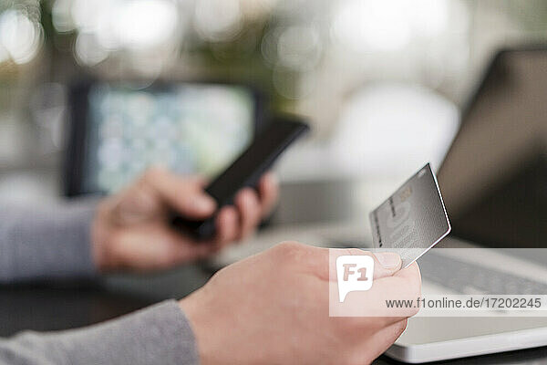 Hände eines Geschäftsmannes beim Online-Bezahlen mit Kreditkarte auf einem Mobiltelefon im Büro