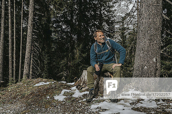 Lächelnder reifer Mann  der eine Wasserflasche hält  während er gegen Bäume im Salzburger Land  Österreich  sitzt