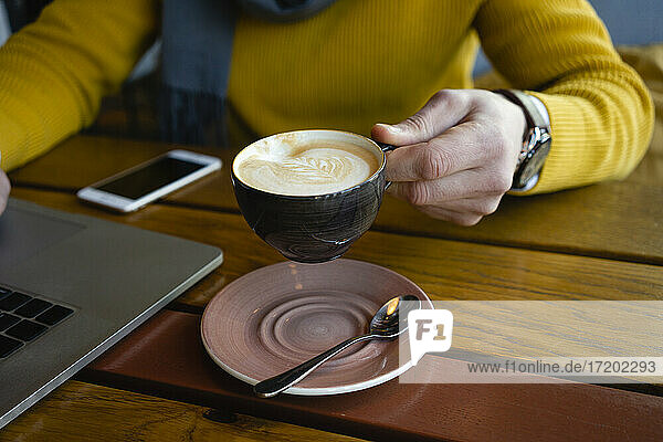 Mann hält Kaffeetasse am Laptop in einem Cafe