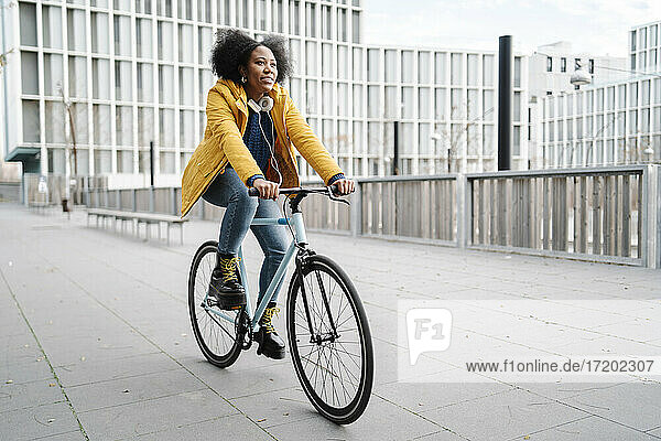 Junge Frau fährt mit dem Fahrrad auf dem Fußweg vor einem Gebäude