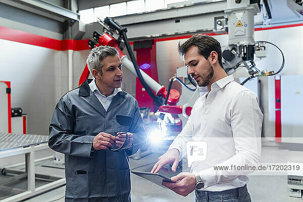 Young male engineer using digital tablet while discussing with mature man in factory