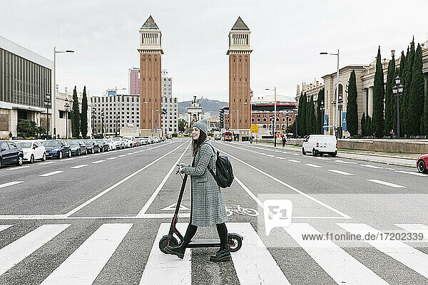 Frau mit Elektroroller beim Überqueren der Straße in der Stadt