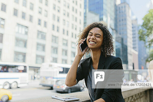 Happy young businesswoman talking on smart phone in city