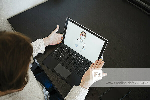 Ältere Frau mit Laptop bespricht sich per Videoanruf mit einem Arzt am Tisch