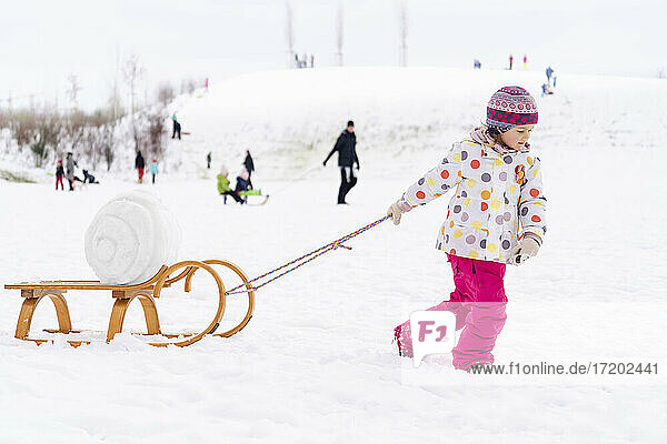 Girl in warm clothing pulling sled on snow at park