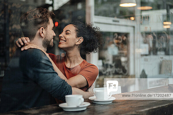 Romantisches Paar lächelnd beim Sitzen mit Arm um einander im Cafe