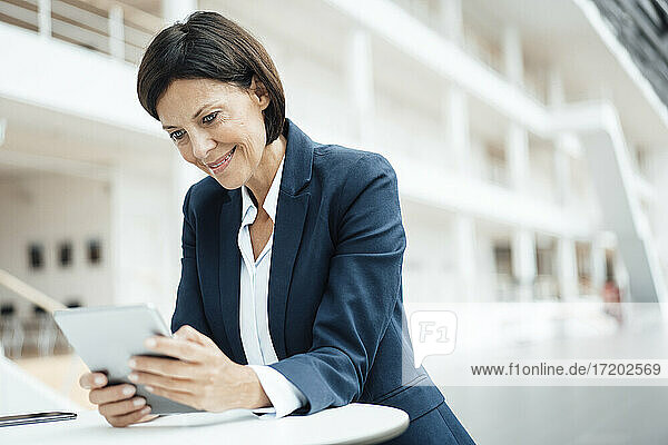 Lächelnde Geschäftsfrau  die bei der Arbeit im Büro ein digitales Tablet benutzt