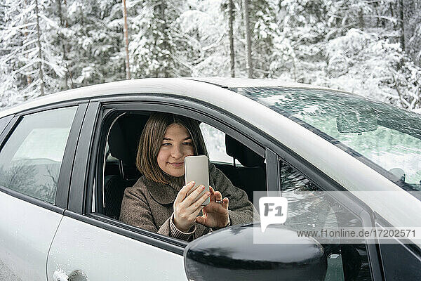 Junge Frau fotografiert im Auto sitzend mit dem Handy