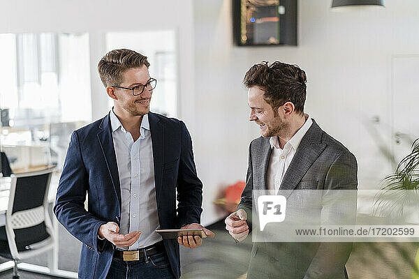 Smiling male entrepreneurs smiling while discussing over digital tablet at creative office