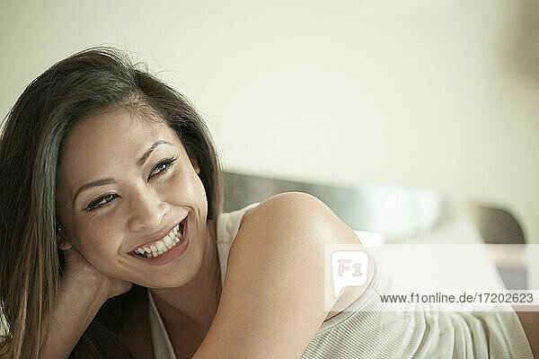 Smiling woman looking away while lying down on bed at home