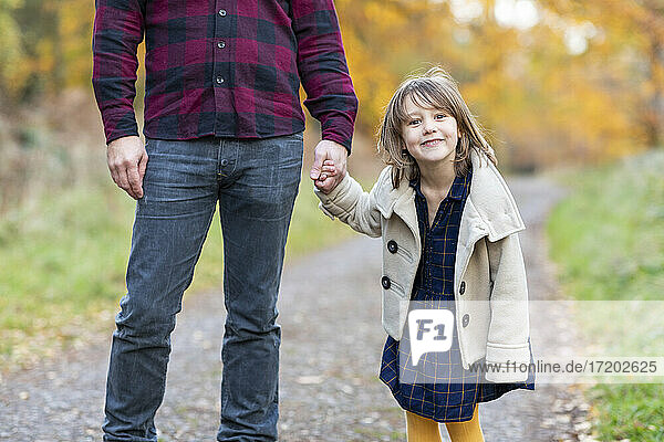 Cute girl smiling while holding father's hand standing in forest