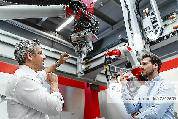 Smiling automation engineers discussing over robot arm in factory