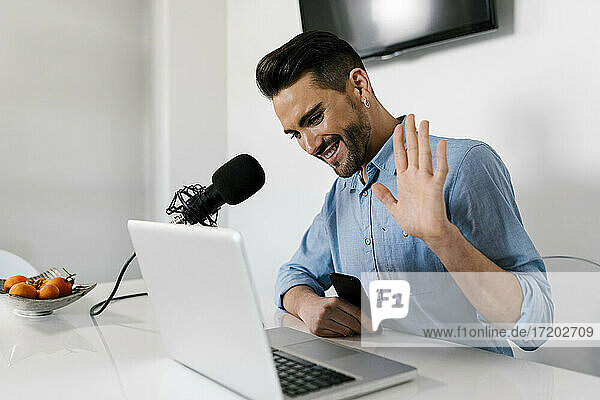 Smiling businessman waving hand on laptop while sitting at home