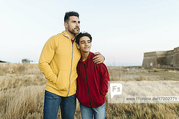 Mann schaut weg  während er seinen Sohn auf dem Feld umarmt