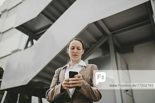 Female business professional text messaging through smart phone against office building