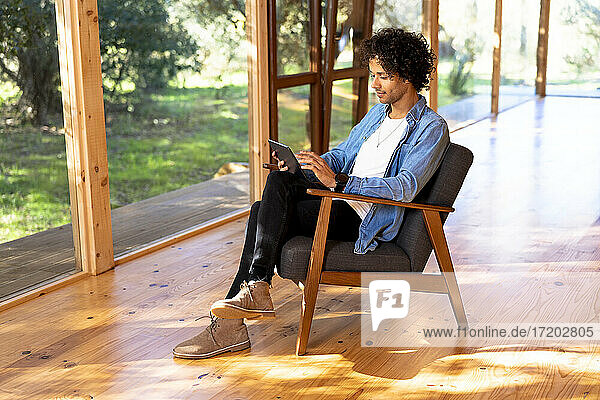 Mann  der ein digitales Tablet benutzt  während er in einem Sessel im Vorgarten sitzt