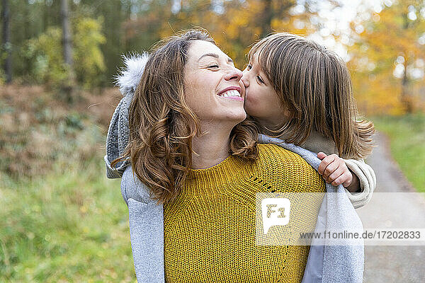 Daughter kissing while piggybacking on mother standing at forest