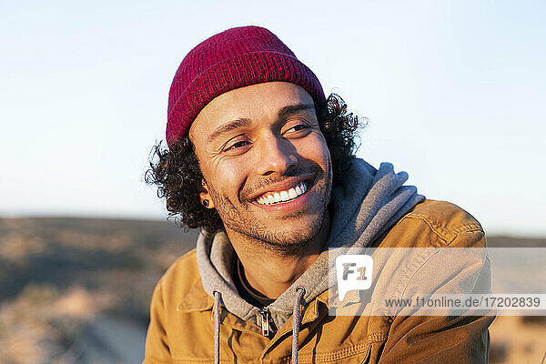 Smiling man wearing knit hat looking away while sitting outdoors
