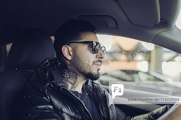 Hipster man in jacket driving car while looking away