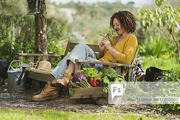 Frau riecht an Salbei und sitzt auf einer Bank im Garten