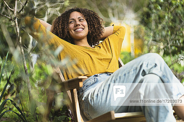 Lächelnde Frau  die sich im Frühling im Gartenstuhl in einem nachhaltigen Bio-Gemüsegarten entspannt