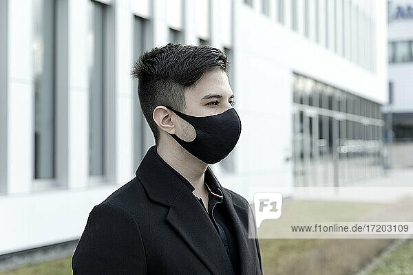 Junger männlicher Unternehmer mit Gesichtsschutzmaske vor einem Bürogebäude