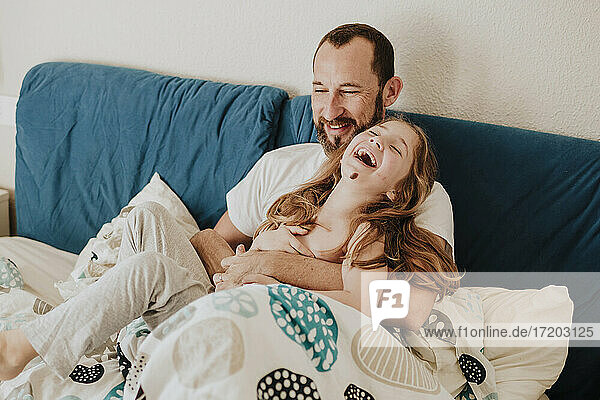 Tochter lacht mit Vater auf dem Bett sitzend