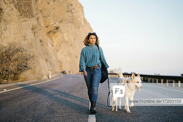 Frau mit Siberian Husky und Jack Russell Terrier schaut weg  während sie auf einer Bergstraße spazieren geht