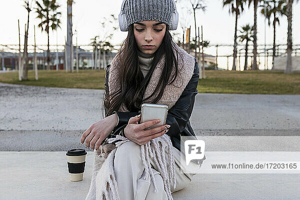 Beautiful teenage girl using smart phone while sitting on bench at park