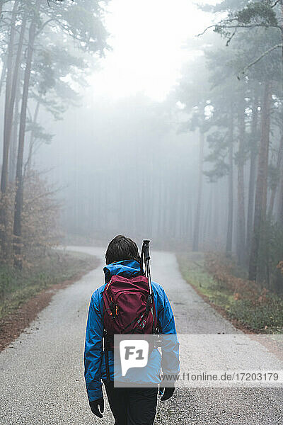 Male backpacker hiking along asphalt road cutting through foggy autumn forest