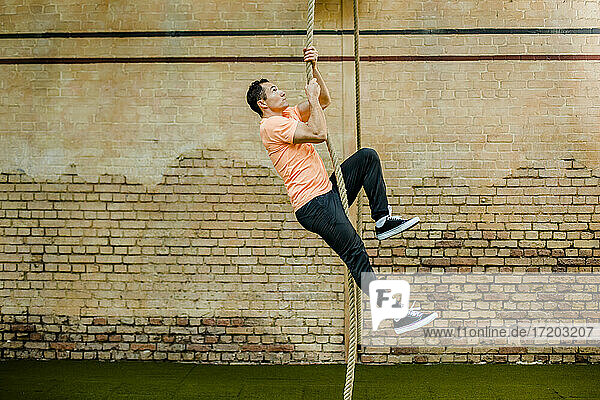 Mann klettert an einem Seil an einer Backsteinmauer im Fitnessstudio