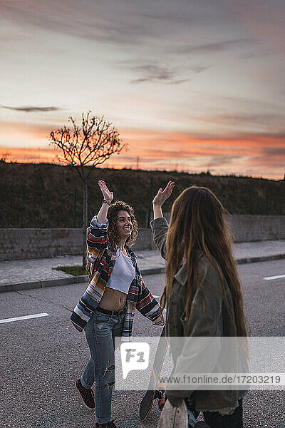 Smiling female friends doing high-five on road during weekend