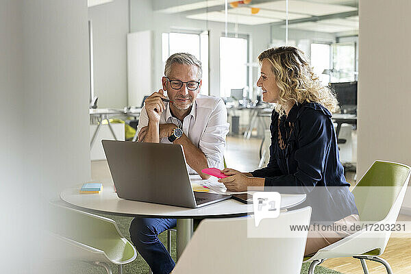 Männlicher und weiblicher Unternehmer mit Laptop am Tisch sitzend während einer Besprechung im Büro