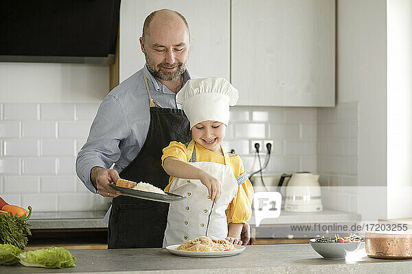 Lächelnde Tochter  die Gewürze ins Essen gibt  während sie in der Küche steht