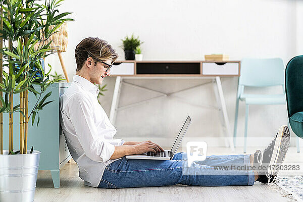 Hübscher junger Mann benutzt Laptop im Wohnzimmer