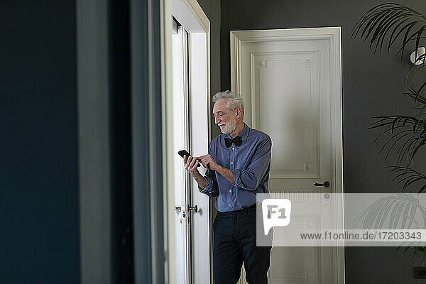 Älterer Mann telefoniert zu Hause am Fenster stehend