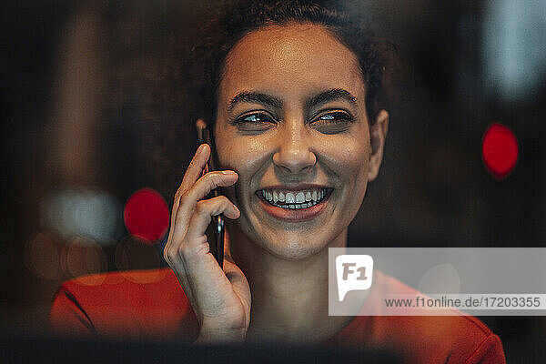 Junge Frau lächelt  während sie in einem Café sitzt und mit ihrem Handy spricht