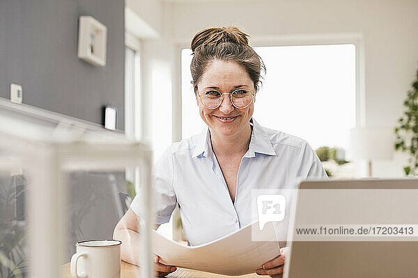 Lächelnde Geschäftsfrau mit Dokument am Schreibtisch sitzend