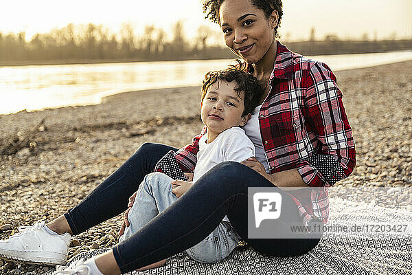 Smiling mother sitting with son on blanket by lake
